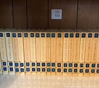 Photo of the complete 21-volume encyclopedia set showing spine labels from A to U including combined letters such as Q-R, with beige hardcovers and gold/blue spine detailing.
