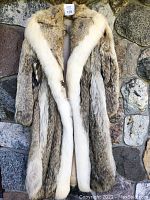 Front view of full length coyote fur coat hanging against stone background