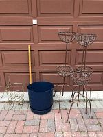 Full view of all six items placed outside in front of brown garage door: three tall metal plant stands with mesh baskets, two smaller decorative vintage metal stands, large blue plastic container.