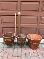 Three wooden planters of varied shapes with metal stands in front of a brown garage door, including a measuring stick for scale.