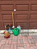 Full view of lot showing plastic and metal watering cans, tomato cages, gardening tools, gloves, terracotta pot with self-watering dish