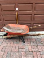 Side view of the full wheelbarrow showing the orange metal tray, wooden handles, flat-free tire, and black metal frame.