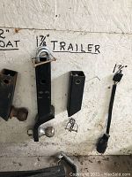 Two trailer hitches, one 2 inch and one 1 7/8 inch with ball mount and clevis pin, hanging on a board labeled with sizes.