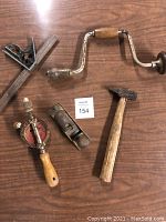 Photo showing hand auger drill, hand planer, chipping hammer, hand drill and metal square arranged on a wooden surface.