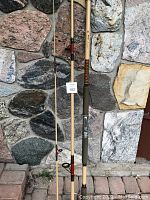 Full view of the 3-piece beige colored fishing rod leaning against a stone wall, shows overall condition and wear.
