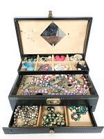 Open view of vintage tiered jewelry box showing three layers: top compartment with earrings and brooches, middle tier with bead and chain necklaces, bottom drawer with assorted earrings.