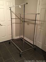 Full view of double adjustable clothing rack showing two horizontal hanging bars on wheels against a beige wall with white doors.