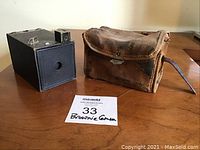 Front view of Kodak Brownie camera and original leather carrying case with visible wear, including banner with seller note 'Brownie Camera'