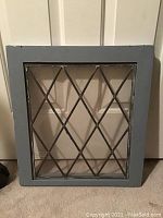 Front view of antique lead glass window showing diamond pattern and grey-blue painted frame