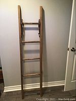 Full view of antique wooden ladder showing tall narrow structure with five round rungs and two side rails.