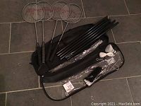 Badminton equipment including four racquets, net posts, net pegs, shuttlecock, and carrying case laid out on floor