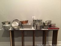 Wide view showing collection of various aluminum bakeware pieces arranged on a table including Bundt, flan, and round pans, plus cookie cutters.