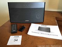 Front view of Bose SoundLink Wireless Music System speaker with remote, stand, and manual on a wood table.