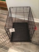 Black wire kennel with door open showing removable bottom tray inside, viewed from above at an angle.