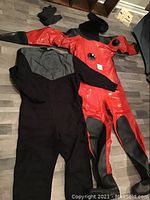 Photo of the flat laid dry suit next to black insulation coveralls with gloves in the background.