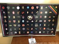 Full view of the framed pin collection showing all pins mounted on black background with edition plaque and colored stripes in top right corner.