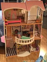 Front view of the three-storey dollhouse showing interior rooms, spiral staircase, and elevator