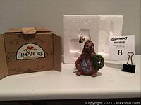 The ornament is a brown dog holding a green wreath with blue and white accents, displayed next to its original brown Jim Shore box and white Styrofoam blob for protection, with MaxSold clip and lot card.