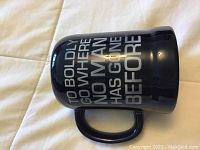 Blue ceramic mug with 'To boldly go where no man has gone before' text in white letters on one side and the Star Trek logo on the other side, placed on a light fabric background.