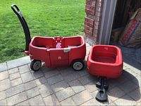 Main red kids wagon with two seats, seatbelts, storage compartment and cup holders shown with attached trailer outside on patio.