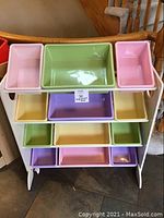Front view of white rack with three tiers of pastel storage buckets in pink, green, yellow, and purple.