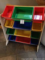 Front view of multiple primary colored plastic storage buckets on a wooden rack, showing red, green, yellow, and blue buckets arranged on three tiers of the rack.