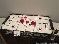Top view of the tabletop air hockey game showing the playing surface and two red paddles and two red pucks.