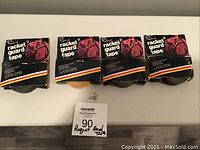 Four rolls of tennis racquet guard tape, three black and one yellow, new in package, displayed on a white surface with a label showing lot number and description.