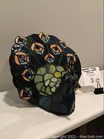 Peacock-shaped Tiffany-style table lamp in daylight, showing colored stained glass detailing.