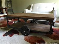 Overall view of industrial style coffee table with wood top, lower shelf, large spoked wheels and caster wheels