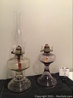 Full view of two antique coal oil lamps side by side on black cloth, clear lamp left, purple lamp right.