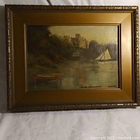 Full view of the antique oil painting displayed in an ornate gilt gold wooden frame, showing the landscape, boats, and castle in the painting, with signature and title visible.