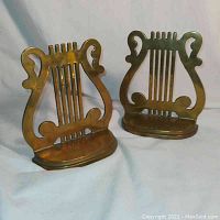 Pair of brass bookends with lyre musical design seen from the front.