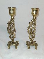 Full front view of pair of brass modernist candlesticks with openwork abstract stems and three-legged bases.