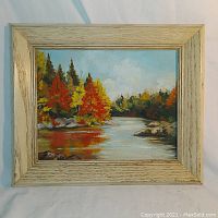 Front view of framed oil painting showing autumn landscape with river and trees reflecting in water.