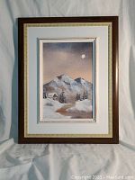 Full view of framed oil painting of snowy mountain landscape under moonlight, featuring a cabin and trees.