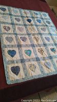 Full view of heart pattern quilt blanket showing grid pattern with heart appliques in blue and floral fabrics on white background with blue sashing.
