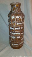 Front view of tall pottery vase showing the bubbly icy lava glaze texture and color variations in brown, white and amber hues.