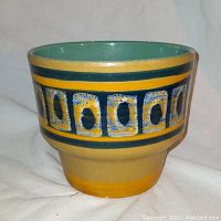 Front view showing the hand painted geometric pattern in teal, yellow, blue, and beige on the ceramic plant pot.
