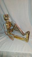 Side view of seated hand carved and painted wooden skeleton puppet with jointed arms and legs showing details of the paint and carving work.