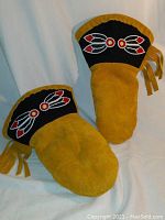 Pair of deerskin gloves showing the front with black beaded feather cuff and fringed sides.