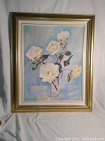 Framed oil painting showing white roses in a glass vase with a gold wood frame.
