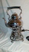 Front view of ornate United USA vintage coffee maker percolator on tilt stand with electric cord visible.
