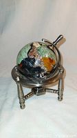 Front view of small gemstone globe showing various colored inlaid countries, mounted on metal stand with three legs and circular frame.