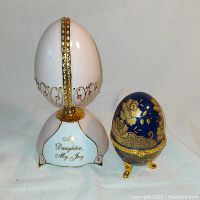 Two porcelain eggs decor, one white jeweled musical egg with 'My Daughter, My Joy' inscription and one cobalt blue and gold Limoges style egg.