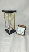 Pair showing Orient travel alarm clock and hourglass sand timer on white background.