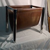 Front and side view showing full vintage magazine rack with chrome legs and brown leather sling.