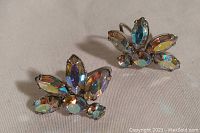 Pair of vintage Sherman clip-on earrings with iridescent blue rhinestones arranged in a floral cluster, lying on flat surface