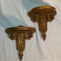 View of two vintage wall shelves with ornate carved design and gold finish.