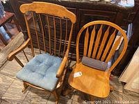 Photo of two wooden chairs: one rocking chair with blue seat cushion and curved back with spindles, one wooden chair with vertical slats back and gray seat cushion.